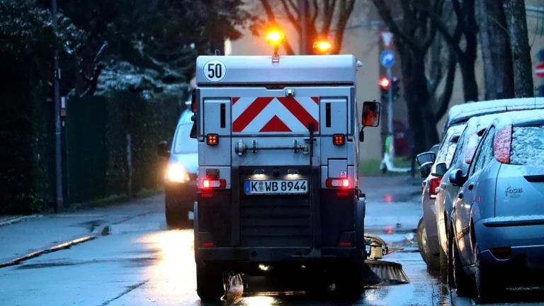 Úklidový vůz čistí večer ulici mezi zaparkovanými auty