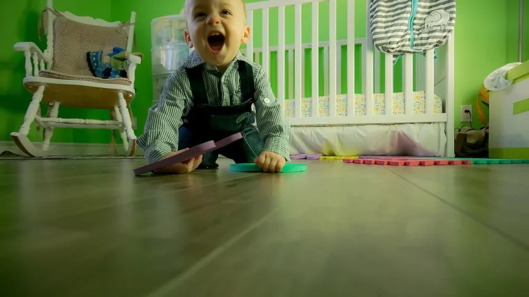 Smějící se batole sedí na podlaze dětského pokoje