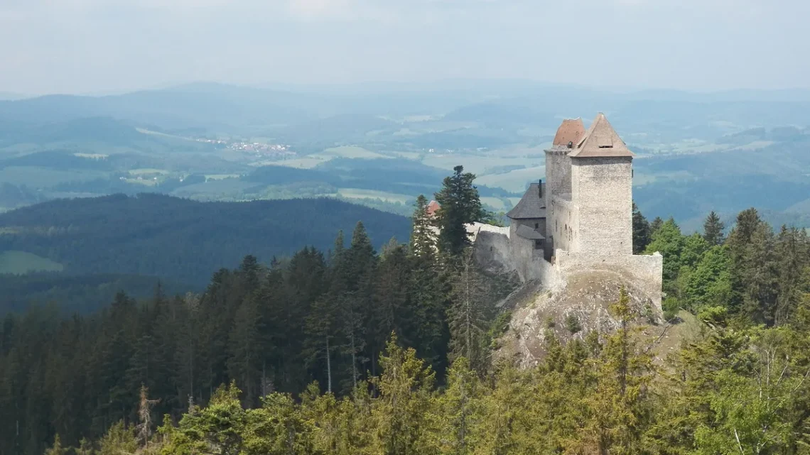Gotický hrad Kašperk se dvěma věžemi na zalesněném kopci nad Šumavou, pohled z Pustého hrádku