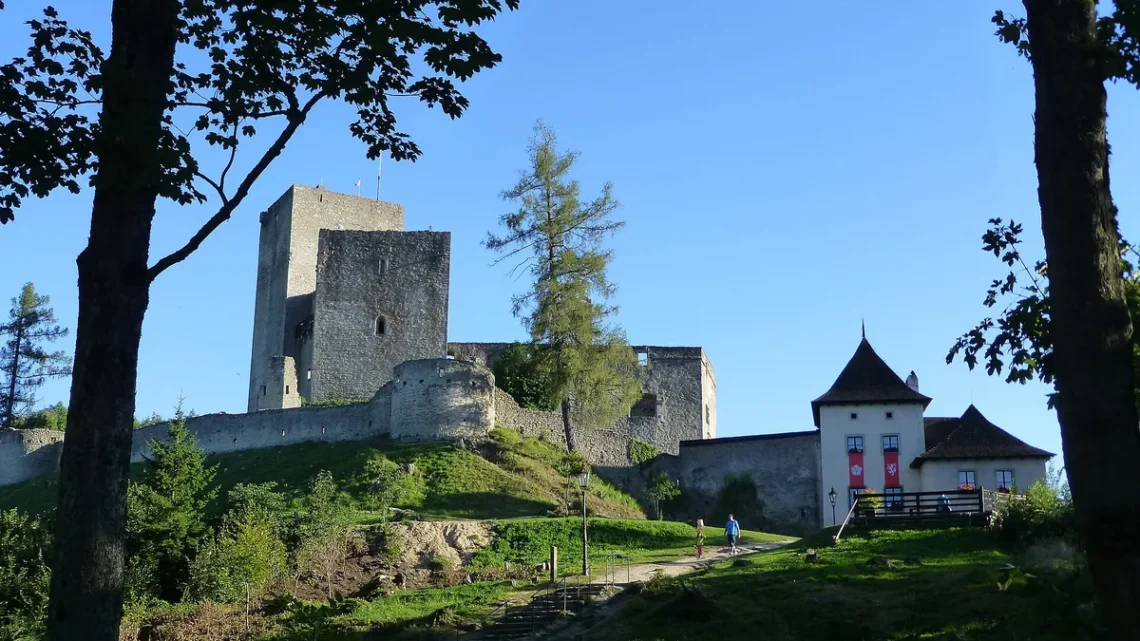 Zřícenina hradu Landštejn s velkou románskou věží, hradbami a bílou vstupní budovou ve večerním slunci
