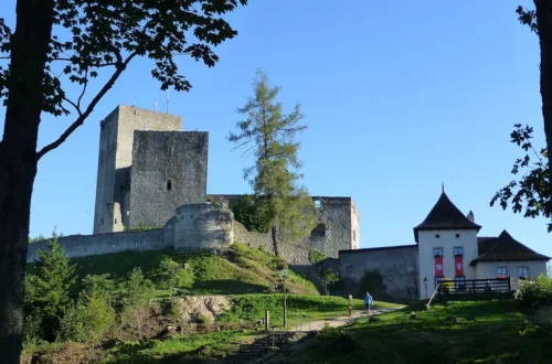 Zřícenina hradu Landštejn s velkou románskou věží, hradbami a bílou vstupní budovou ve večerním slunci