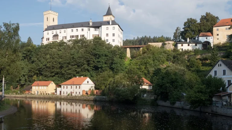 Bílý hrad Rožmberk s hranolovou věží nad řekou Vltavou a domy na břehu v Rožmberku nad Vltavou
