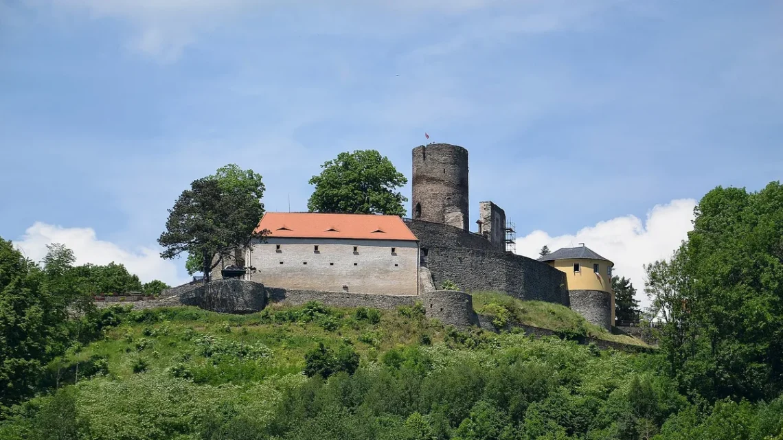 Hrad Svojanov s válcovou věží a palácem s červenou střechou nad zalesněným svahem