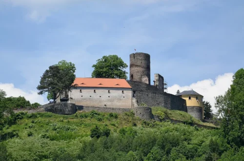 Hrad Svojanov s válcovou věží a palácem s červenou střechou nad zalesněným svahem