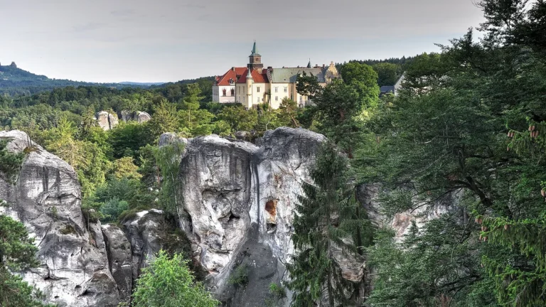 Zámek Hrubá Skála nad pískovcovými věžemi Hruboskalska, v pozadí vlevo zřícenina Trosky