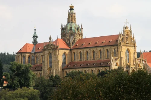 Kostel Nanebevzetí Panny Marie v klášteře Kladruby s kopulí a zlacenou korunou nad korunami stromů