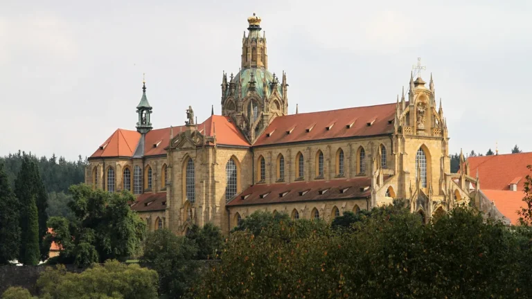 Kostel Nanebevzetí Panny Marie v klášteře Kladruby s kopulí a zlacenou korunou nad korunami stromů