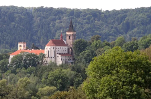 Sázavský klášter s kostelem sv. Prokopa a gotickou věží nad zalesněným údolím řeky Sázavy
