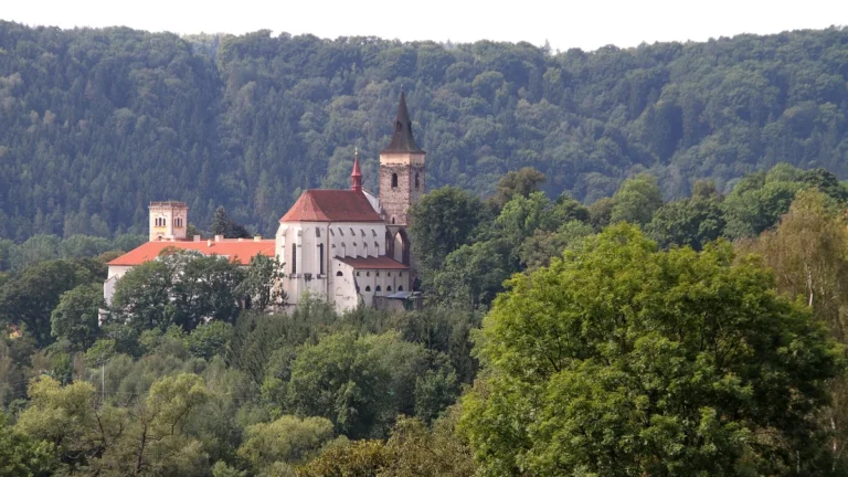 Sázavský klášter s kostelem sv. Prokopa a gotickou věží nad zalesněným údolím řeky Sázavy