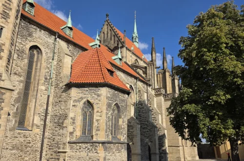 Kamenná boční stěna chrámu sv. Bartoloměje v Kolíně s červenou střechou kaple a gotickými věžičkami chóru