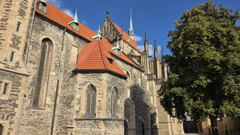 Kamenná boční stěna chrámu sv. Bartoloměje v Kolíně s červenou střechou kaple a gotickými věžičkami chóru