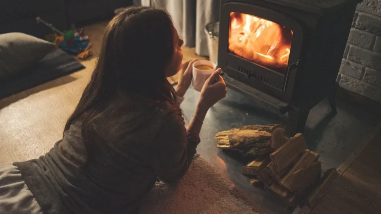 Žena leží u kamen s hořícím ohněm a hrnkem