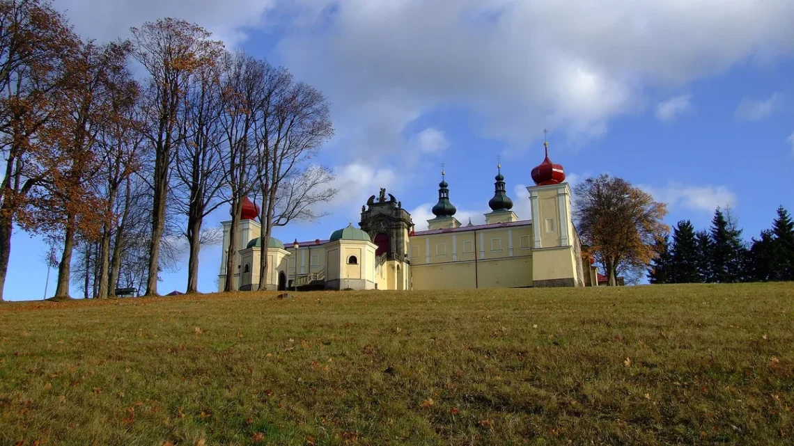 Barokní poutní areál Hora Matky Boží nad Králíky s věžemi kostela a ambity za podzimní alejí