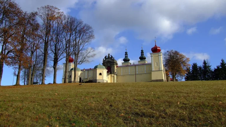 Barokní poutní areál Hora Matky Boží nad Králíky s věžemi kostela a ambity za podzimní alejí