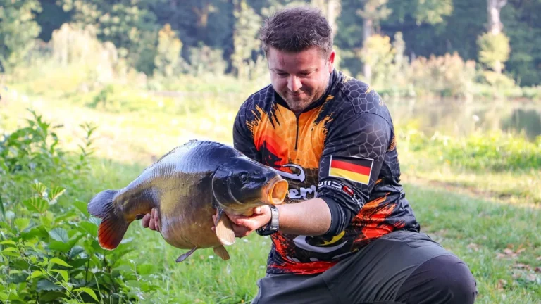 Rybář kleká u vody a drží velkého kapra