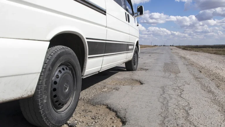 Bílé auto stojí na rozbité silnici s výmolem