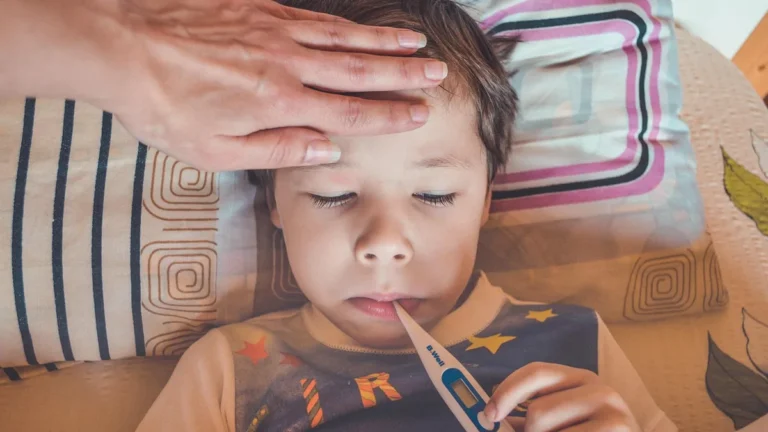 Nemocný chlapec s teploměrem a rukou na čele