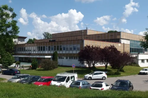 Budova krytého plaveckého bazénu v Kroměříži s prosklenou halou a hnědou obkladovou fasádou, před ní parkoviště s auty a trávník