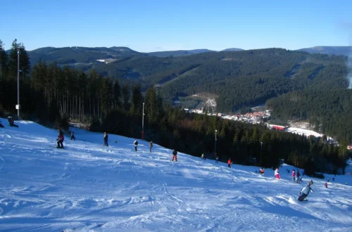 Lyžaři na zasněžené sjezdovce ve skiareálu Bílá s výhledem do zalesněného údolí Beskyd