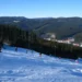 Lyžaři na zasněžené sjezdovce ve skiareálu Bílá s výhledem do zalesněného údolí Beskyd
