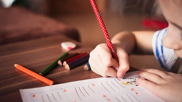 Dítě vybarvuje tužkami pracovní list u stolu