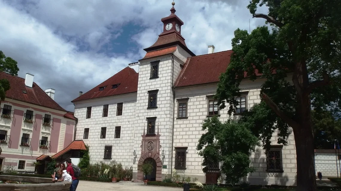 Nádvoří renesančního zámku Třeboň s hodinovou věží, kamennou kašnou a vzrostlým stromem