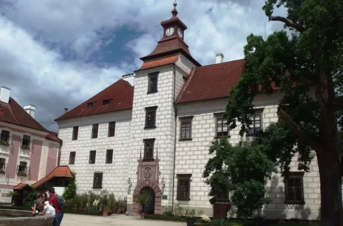 Nádvoří renesančního zámku Třeboň s hodinovou věží, kamennou kašnou a vzrostlým stromem