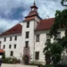 Nádvoří renesančního zámku Třeboň s hodinovou věží, kamennou kašnou a vzrostlým stromem
