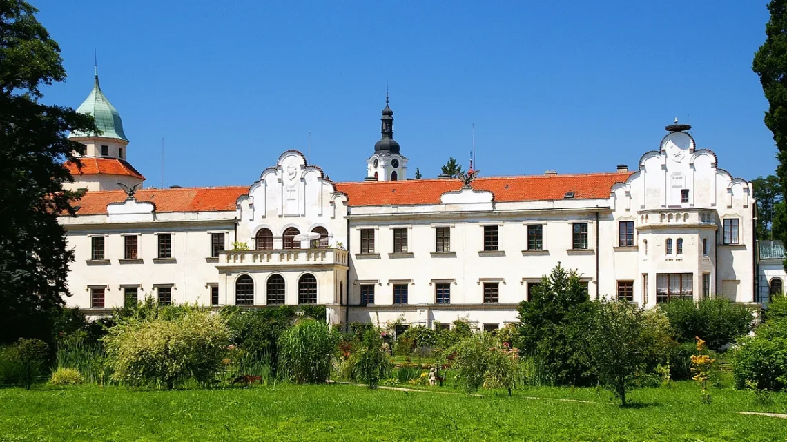 Bílé průčelí zámku Častolovice se štíty a věží se zelenou bání, v popředí zámecký park