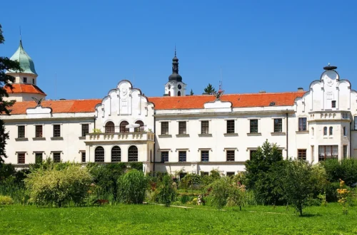 Bílé průčelí zámku Častolovice se štíty a věží se zelenou bání, v popředí zámecký park