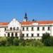 Bílé průčelí zámku Častolovice se štíty a věží se zelenou bání, v popředí zámecký park