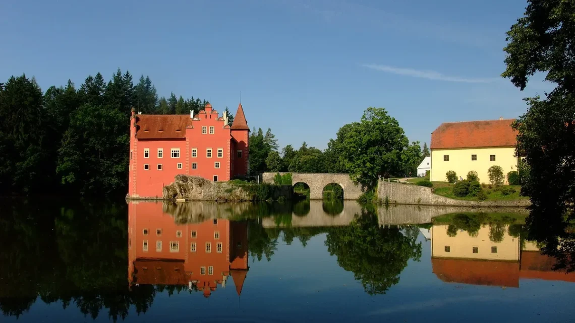 Červený zámek Červená Lhota na skále v rybníce s kamenným mostem a odrazem ve vodě