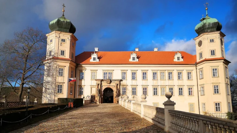 Vstupní průčelí zámku Mníšek pod Brdy se dvěma věžemi a dlážděným mostem