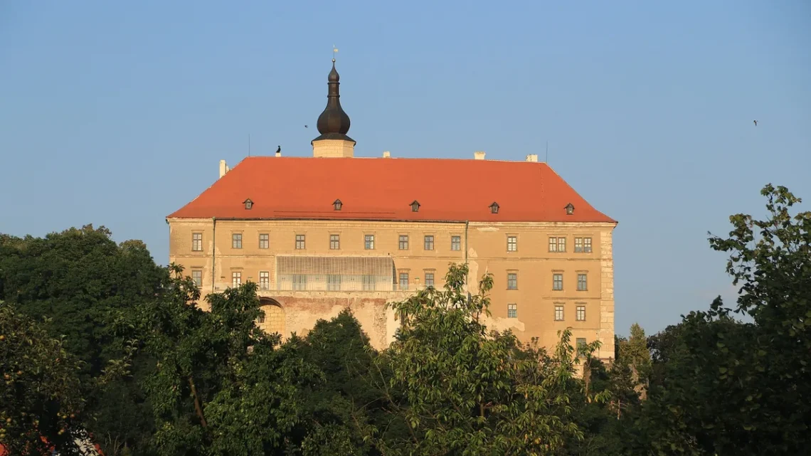Zámek Náměšť nad Oslavou s červenou střechou a věží nad korunami stromů