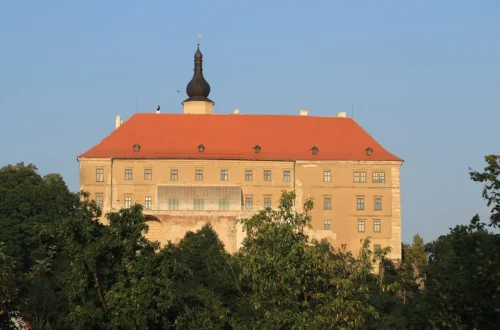 Zámek Náměšť nad Oslavou s červenou střechou a věží nad korunami stromů