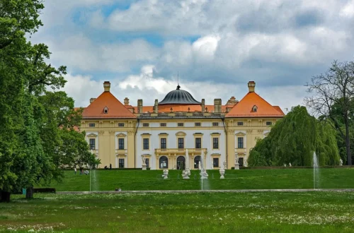 Zahradní průčelí barokního zámku Slavkov u Brna s fontánami a sochami v zámeckém parku