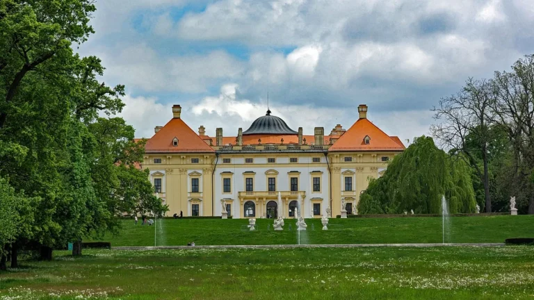 Zahradní průčelí barokního zámku Slavkov u Brna s fontánami a sochami v zámeckém parku