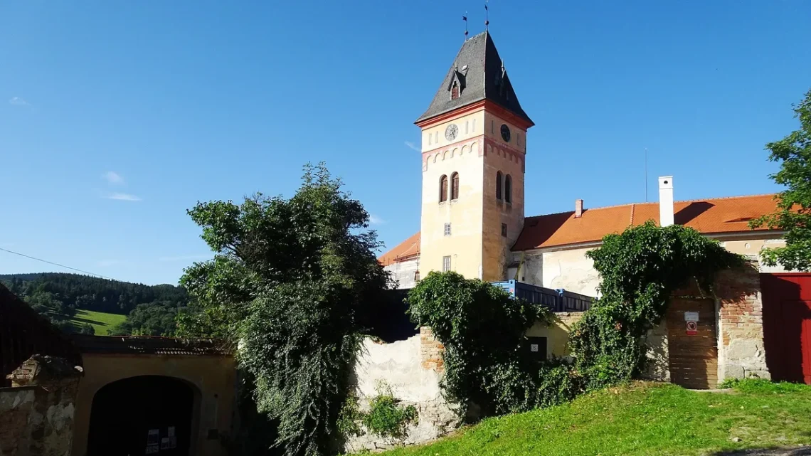 Hodinová věž zámku Vimperk nad zeleným svahem a hradbami