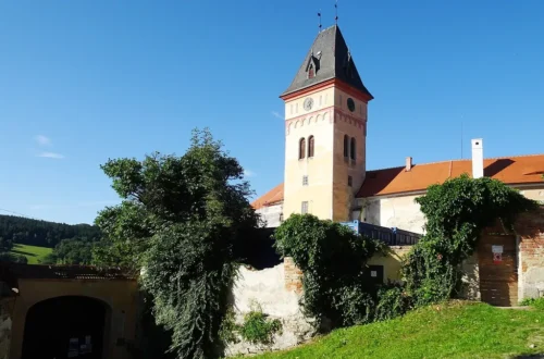 Hodinová věž zámku Vimperk nad zeleným svahem a hradbami