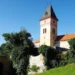 Hodinová věž zámku Vimperk nad zeleným svahem a hradbami