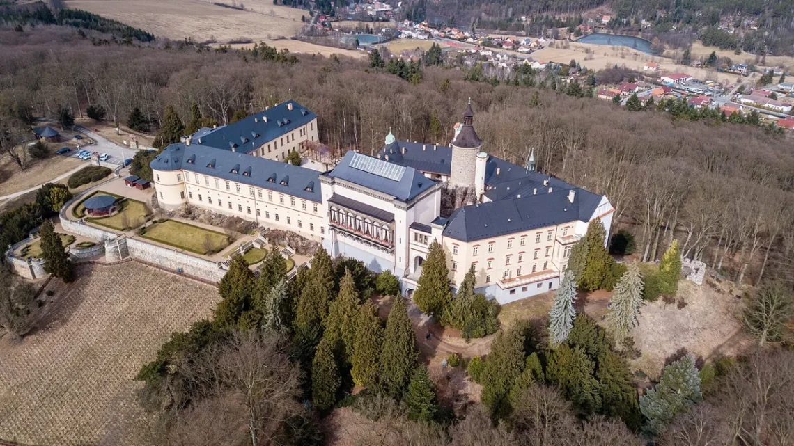 Letecký pohled na zámek Zbiroh na skalním ostrohu s vinicí a městem Zbiroh v pozadí