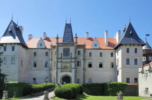 Romantický zámek Žleby, hlavní průčelí s věžemi a vstupní branou nad zámeckým trávníkem