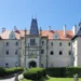 Romantický zámek Žleby, hlavní průčelí s věžemi a vstupní branou nad zámeckým trávníkem