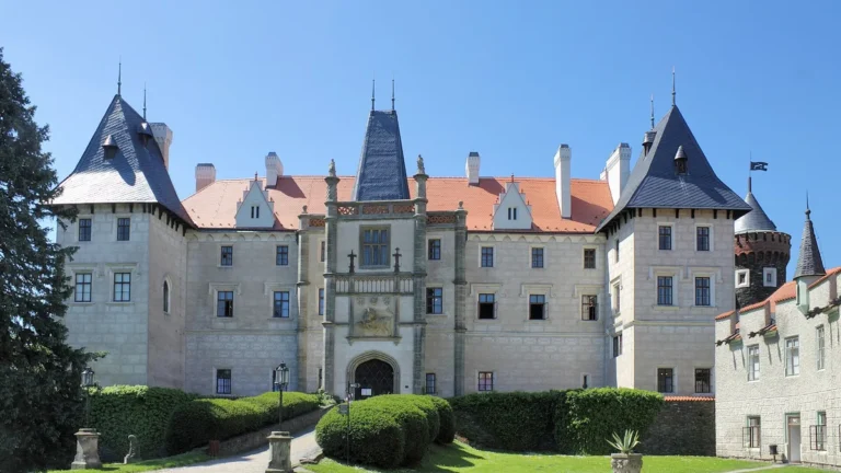 Romantický zámek Žleby, hlavní průčelí s věžemi a vstupní branou nad zámeckým trávníkem