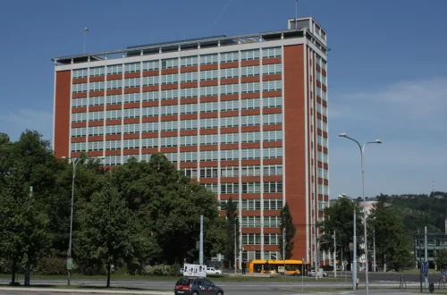 Baťův mrakodrap, budova 21 ve Zlíně, cihlová výšková budova s pásy oken za stromy na třídě Tomáše Bati