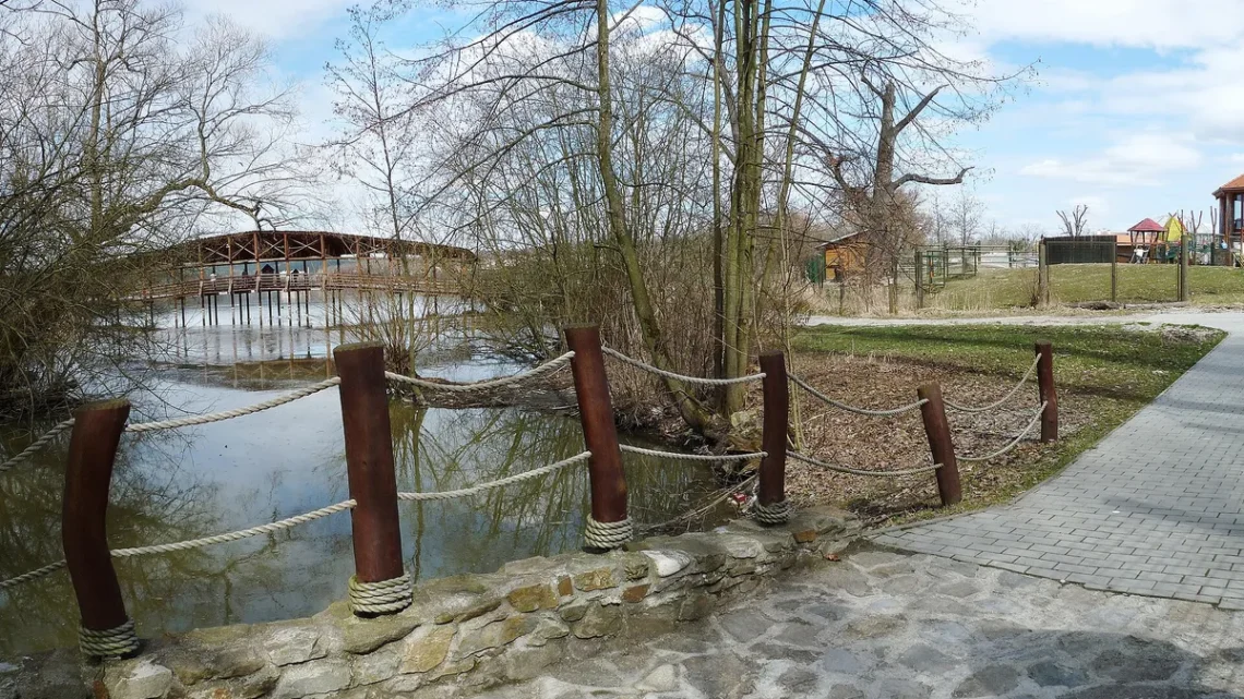 Západní část Zoo Ohrada v Hluboké nad Vltavou s dřevěnou lávkou přes rybník a dlážděnou cestou podél vody