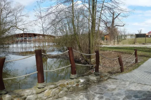 Západní část Zoo Ohrada v Hluboké nad Vltavou s dřevěnou lávkou přes rybník a dlážděnou cestou podél vody